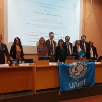 Persone al tavolo del convegno con diapositiva proiettata e bandiera di Unicef